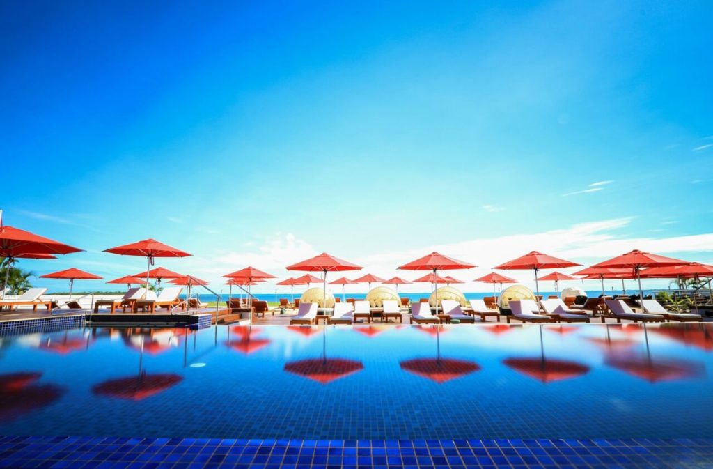 Bright blue sky over a long pool lined with chairs and umbrellas